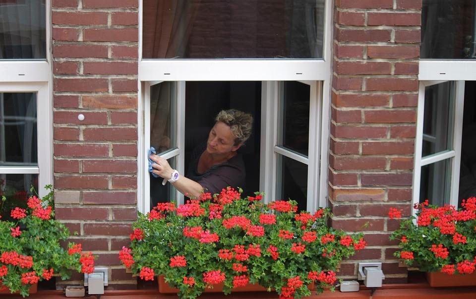 Woman cleaning exterior of window from inside city apartment