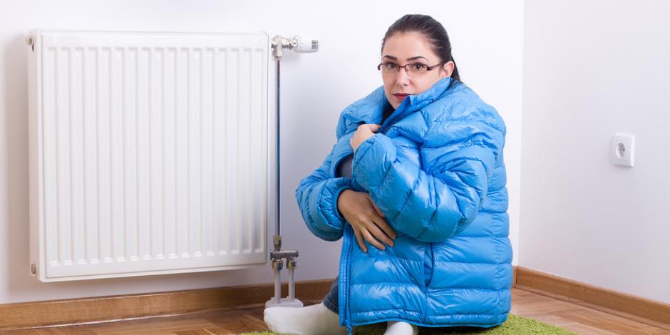 Woman sitting on floor in front of radiator with winter coat on